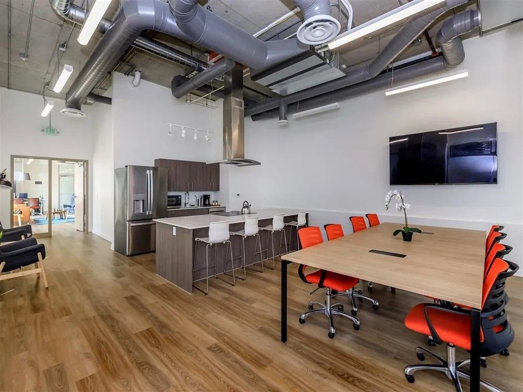 Modern office kitchen and meeting area with a long table, chairs, and a kitchen island with bar stools.