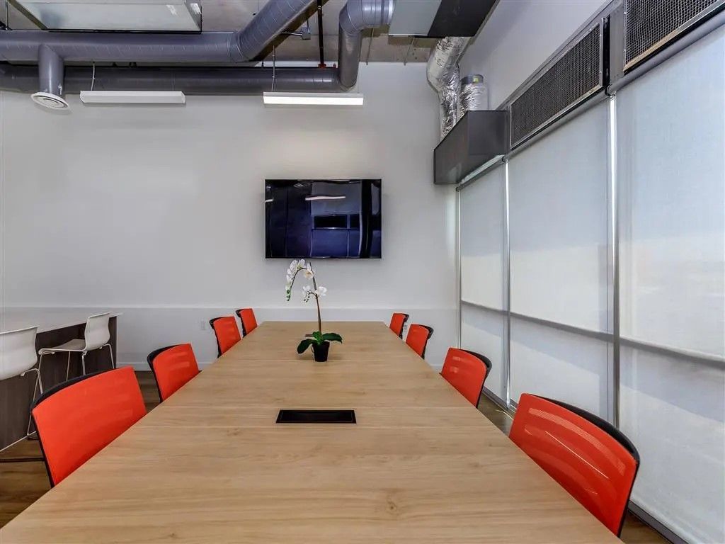 Conference room with long wooden table, orange chairs, and a TV on the wall.