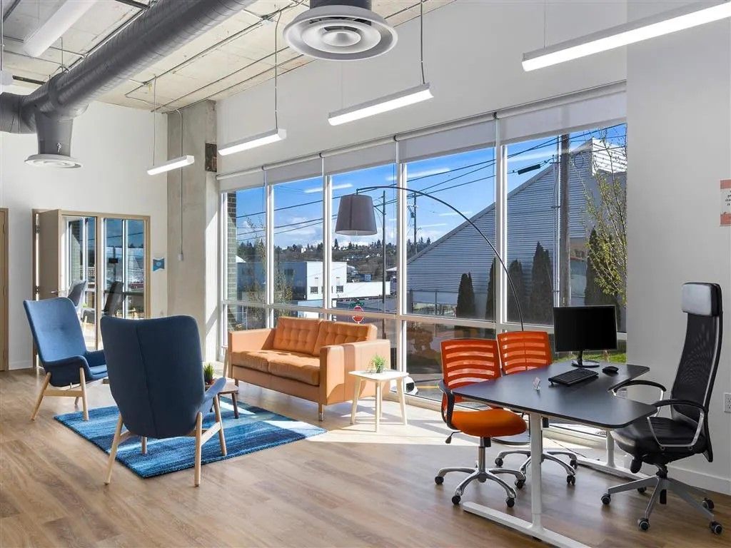 Bright office space with seating, desk, and large windows overlooking outdoors.