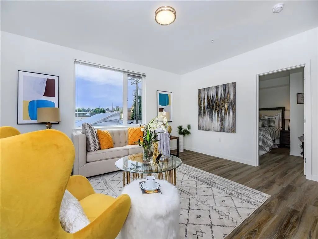 Living room with yellow chair, beige sofa, modern art, and a view through a window.