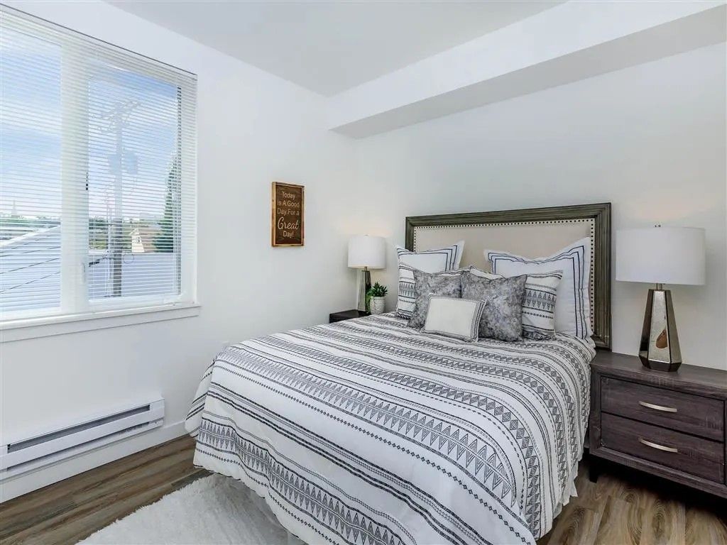 Bedroom with white walls, window with blinds, bed with patterned cover, and nightstands.