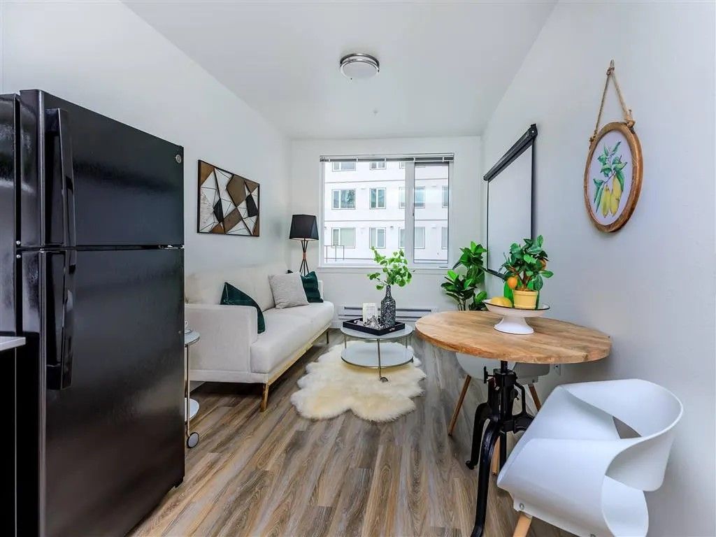Small apartment living room with white walls, black refrigerator, and round table.