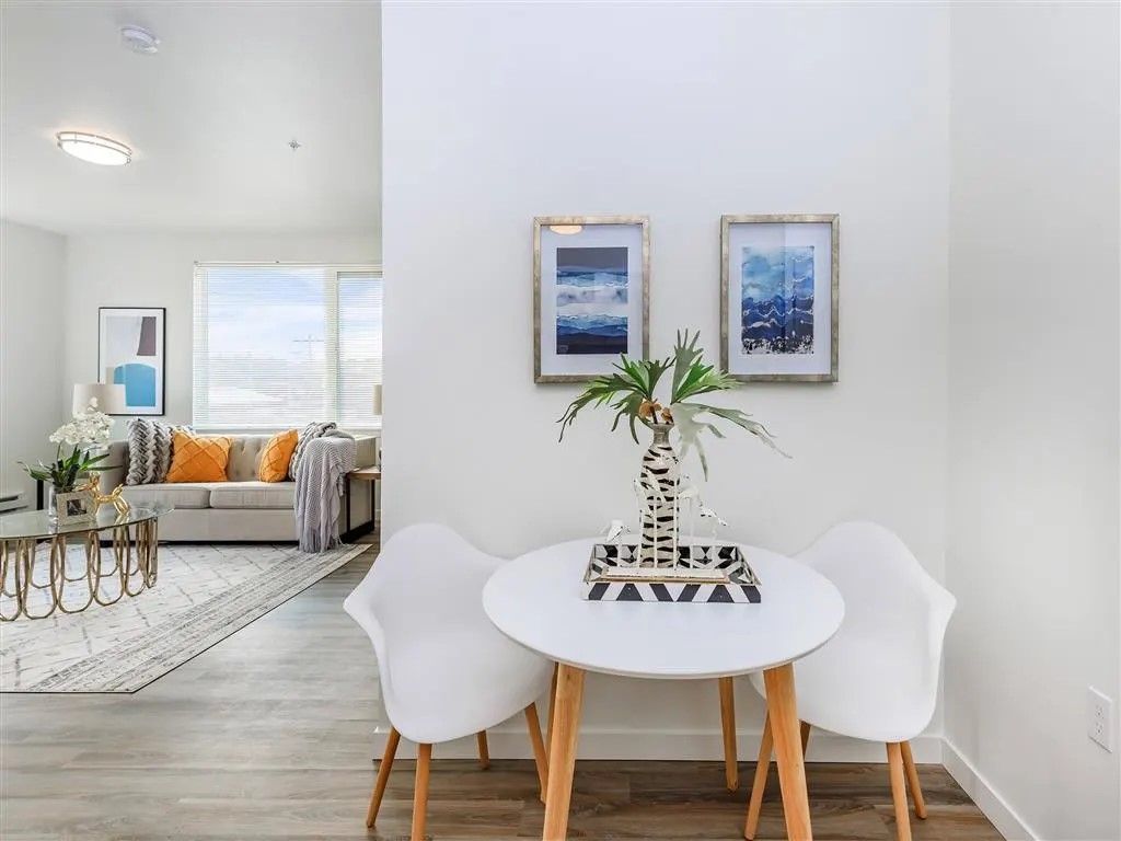 White table with two chairs, two framed paintings, and a plant, in a bright modern home.