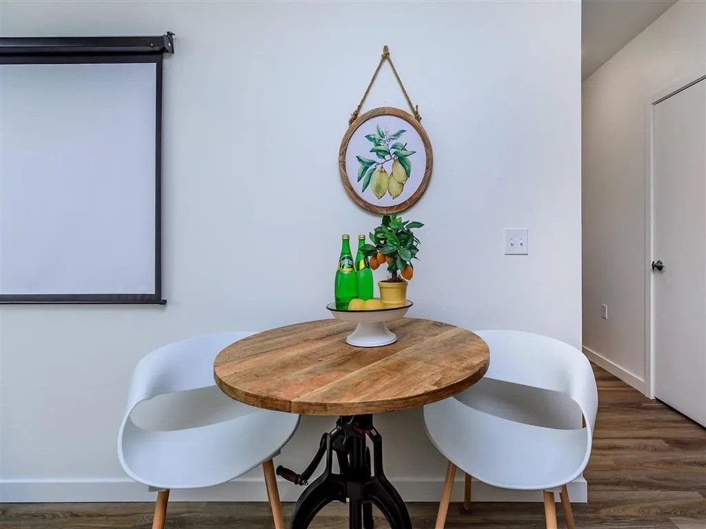 Small round wooden table with two white chairs, decorated with plants and a framed picture.