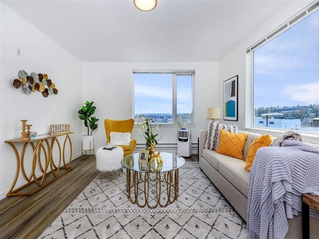 Living room with white walls, sofa, patterned rug, yellow armchair, and city view.