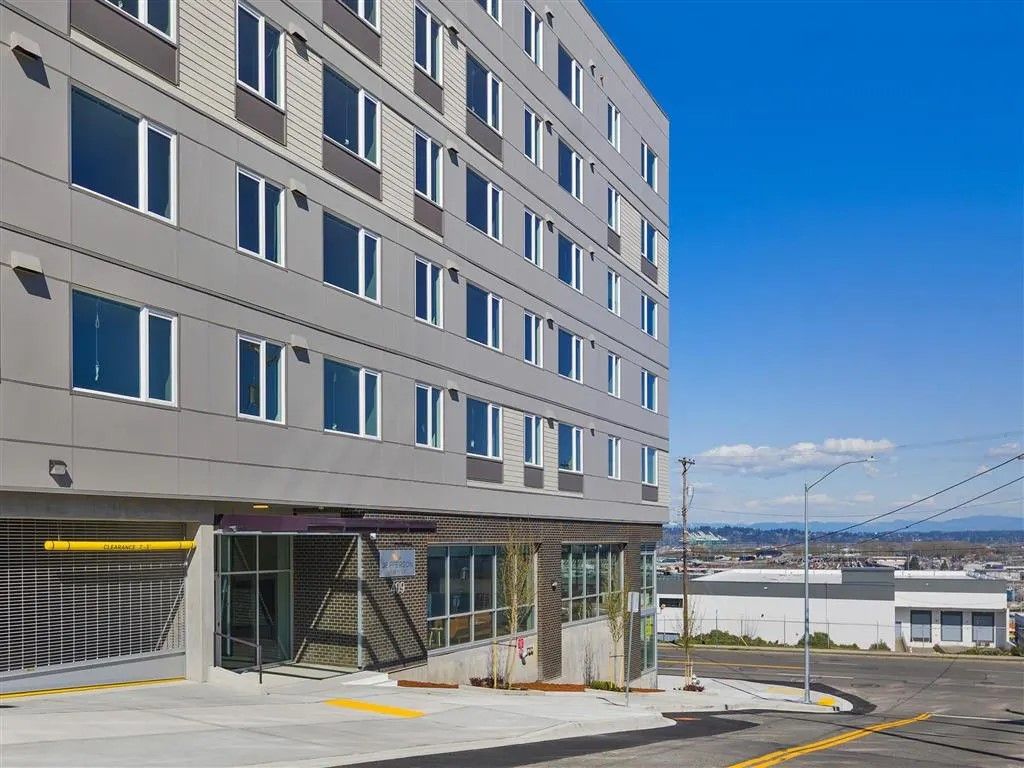 Modern gray building with many windows, glass storefront, and clear blue sky.