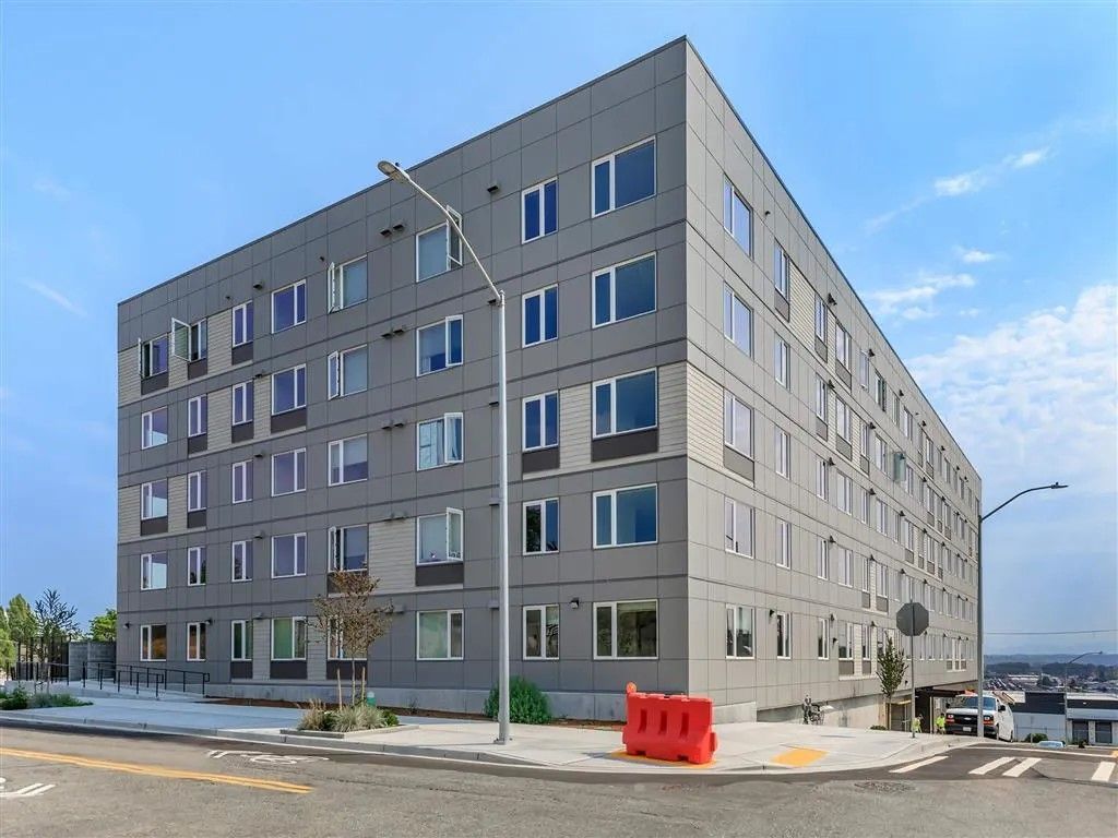 Gray apartment building on a street with a blue sky.