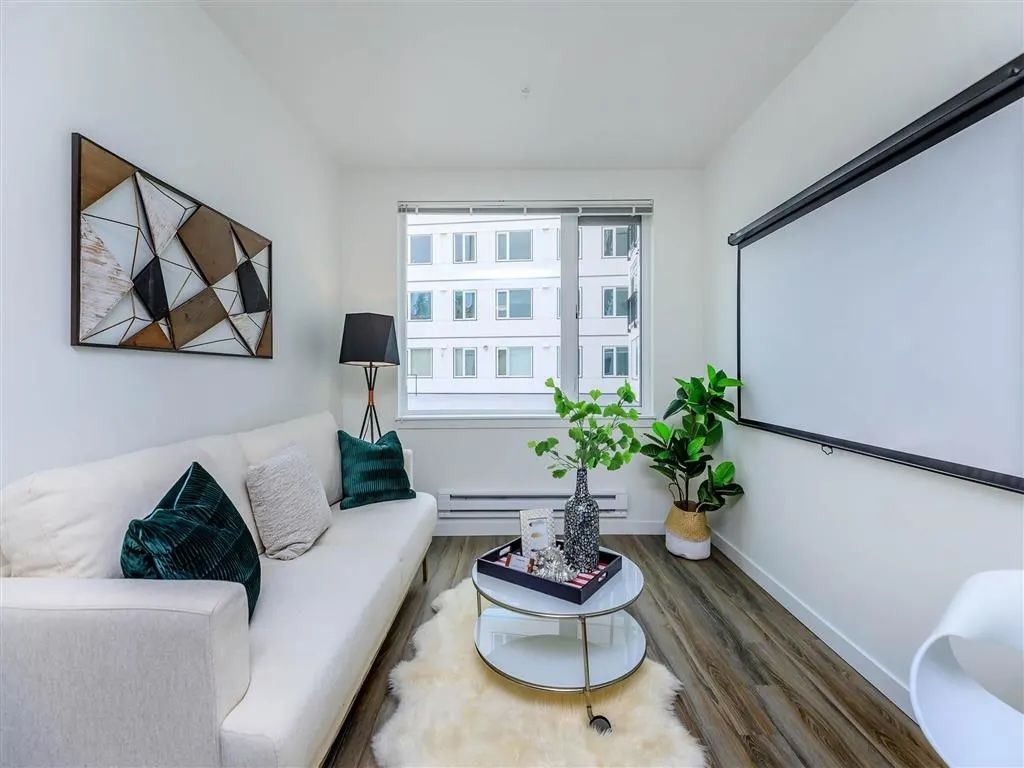 Small living room with white couch, projector screen, window, and decorative art.