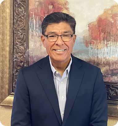 Man in suit and glasses smiles in front of a painting with brown, gold, and orange tones.