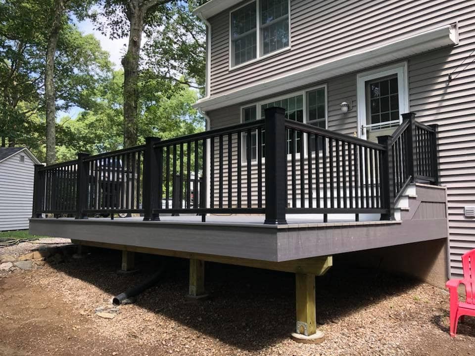 A large deck with a black railing is in front of a house.