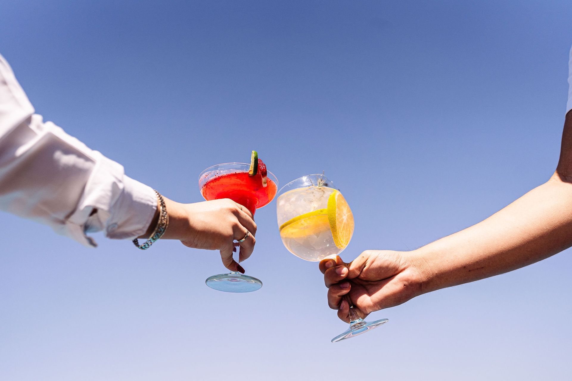A man and a woman are toasting with cocktails against a blue sky.