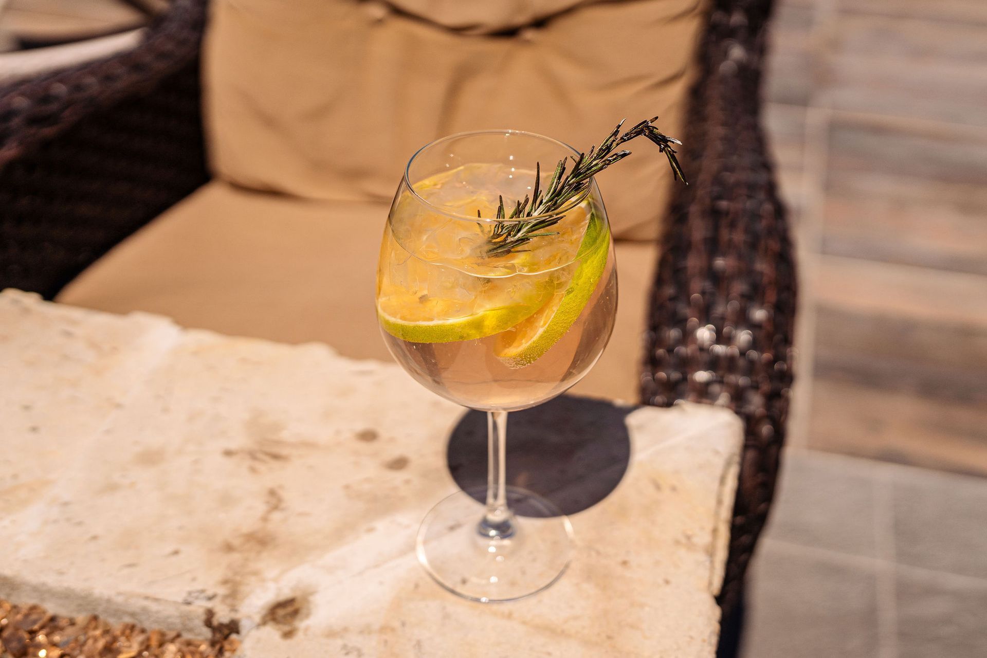 A glass of wine with a slice of lemon and rosemary on a table.