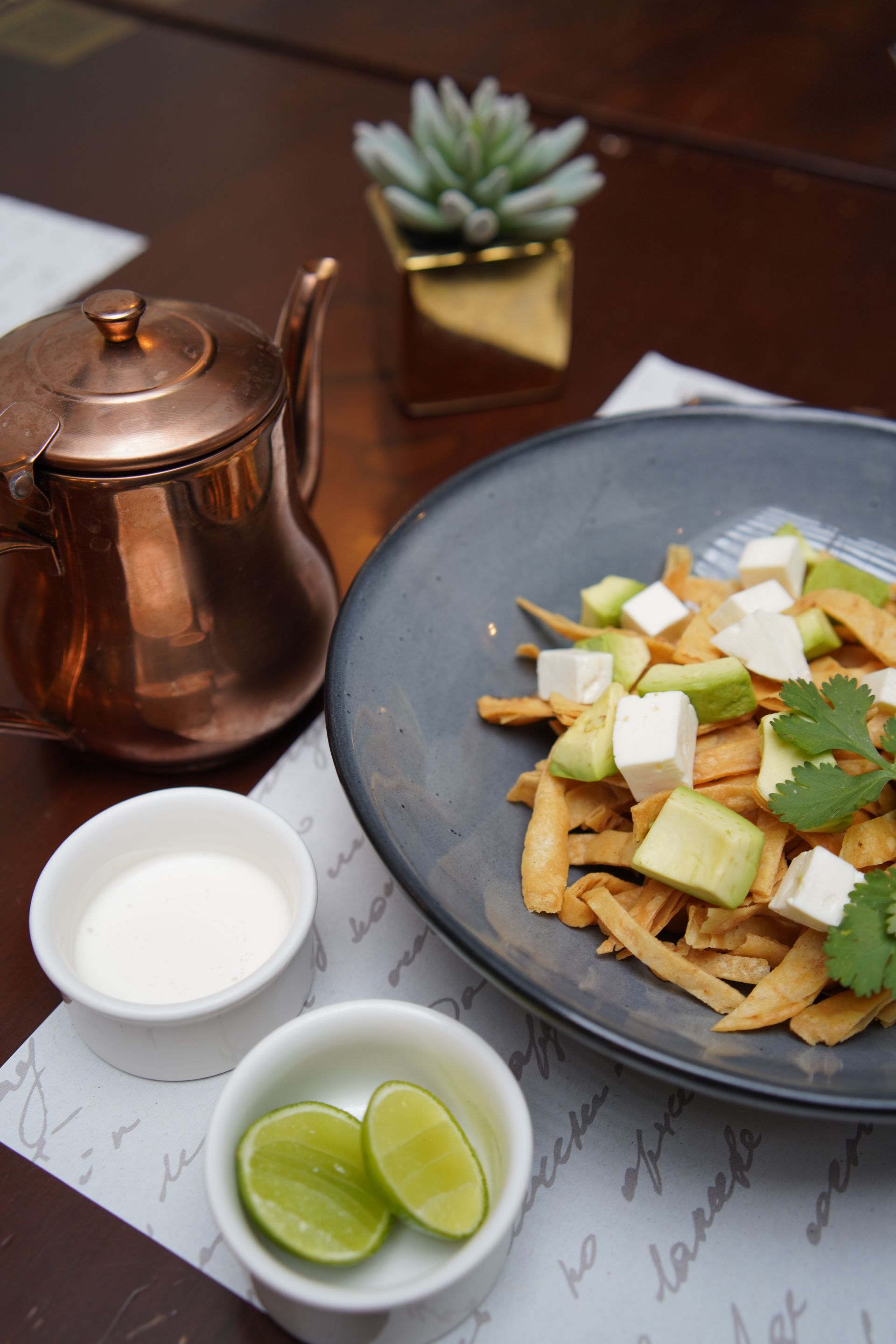 A plate of food is sitting on a table next to a copper teapot.