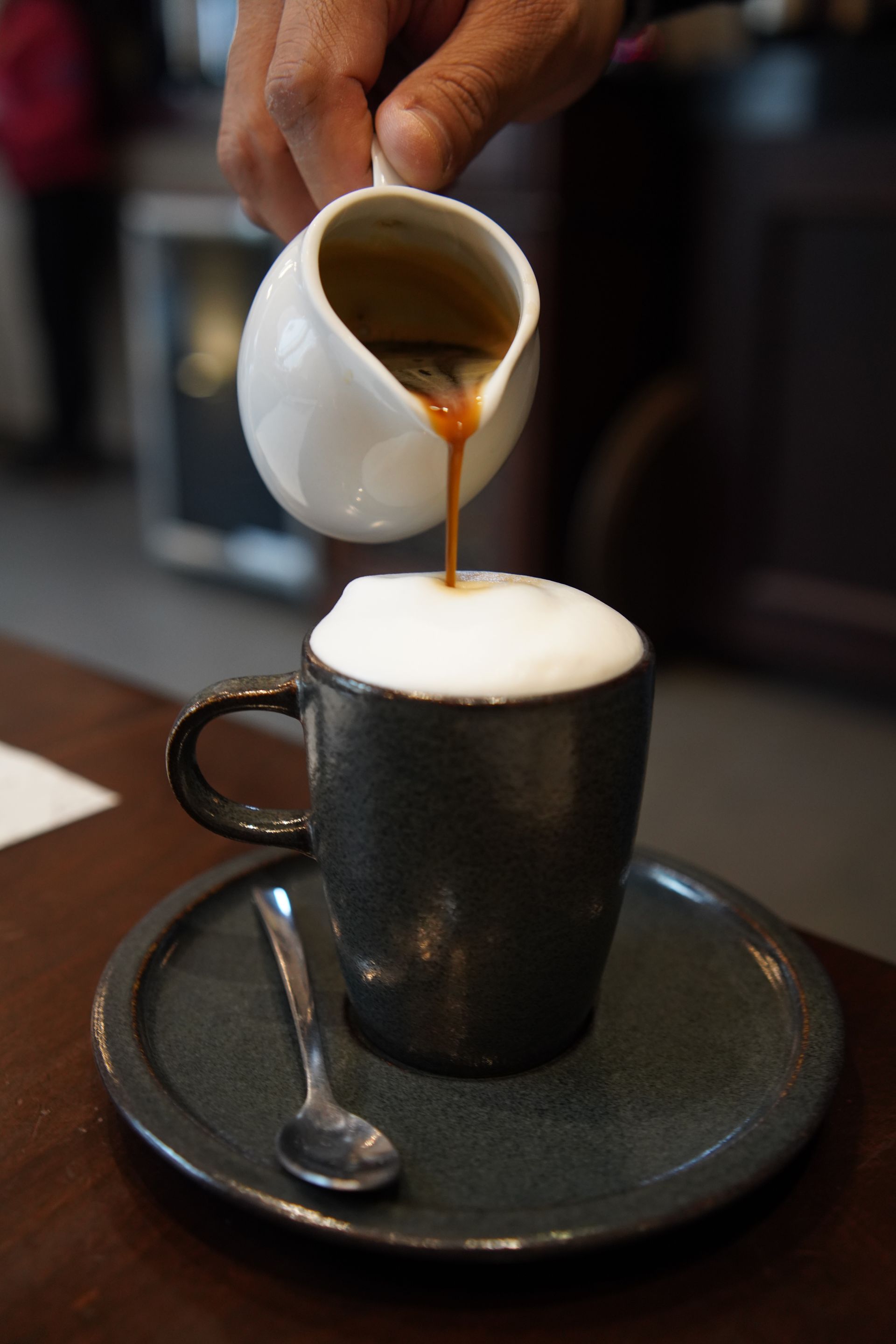 A cup of coffee is being poured into a saucer with a spoon