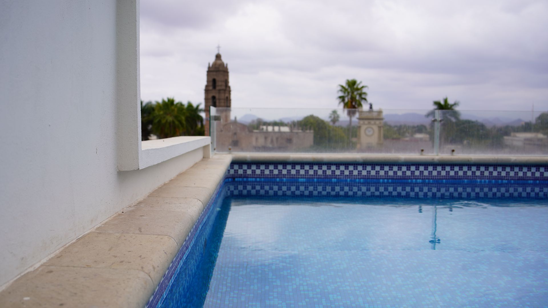 A swimming pool with a view of a city on a cloudy day.