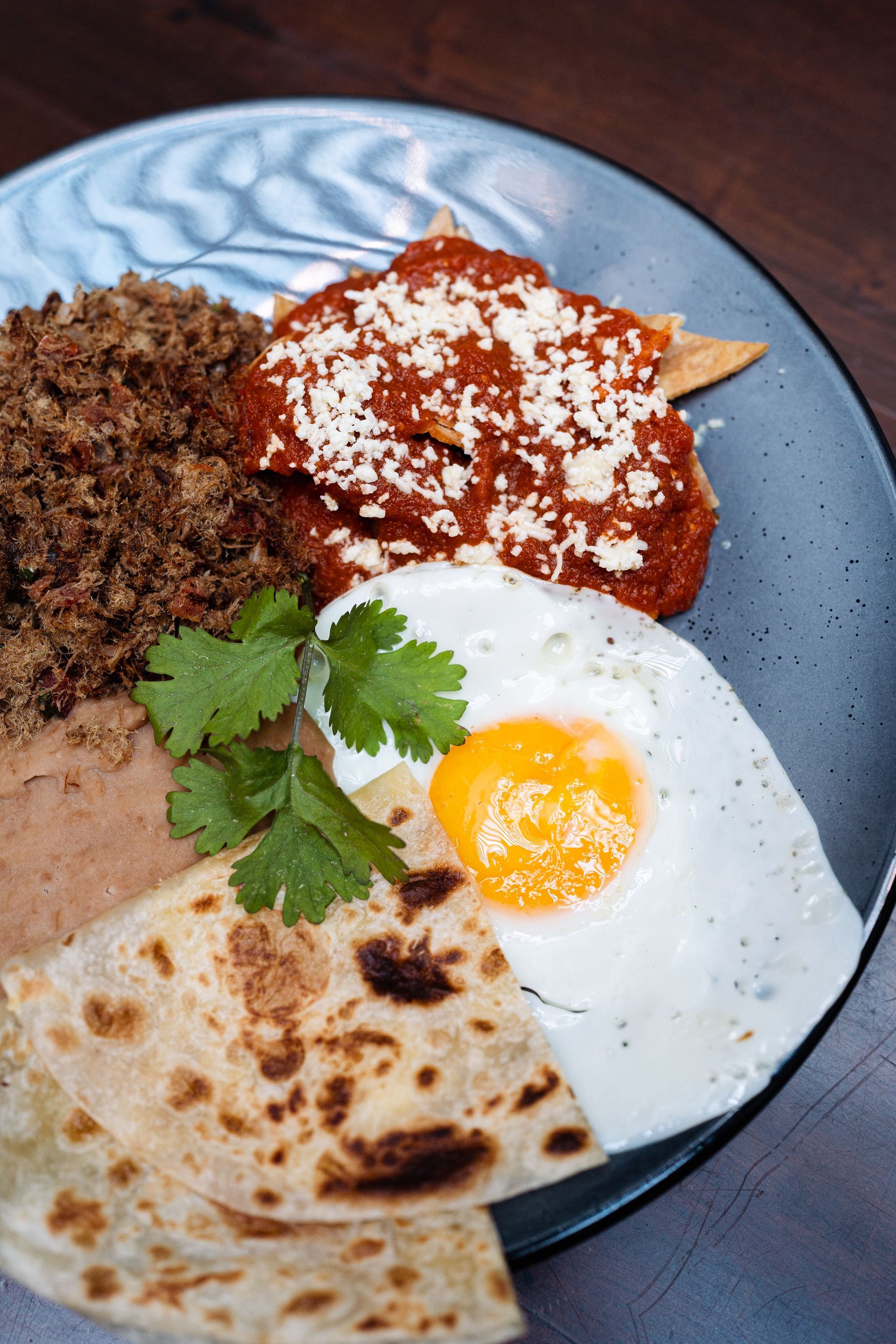 A close up of a plate of food with eggs , tortilla chips , and sauce on a table.