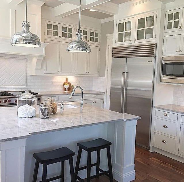 A kitchen with white cabinets , stainless steel appliances , a large island with two stools and a refrigerator.