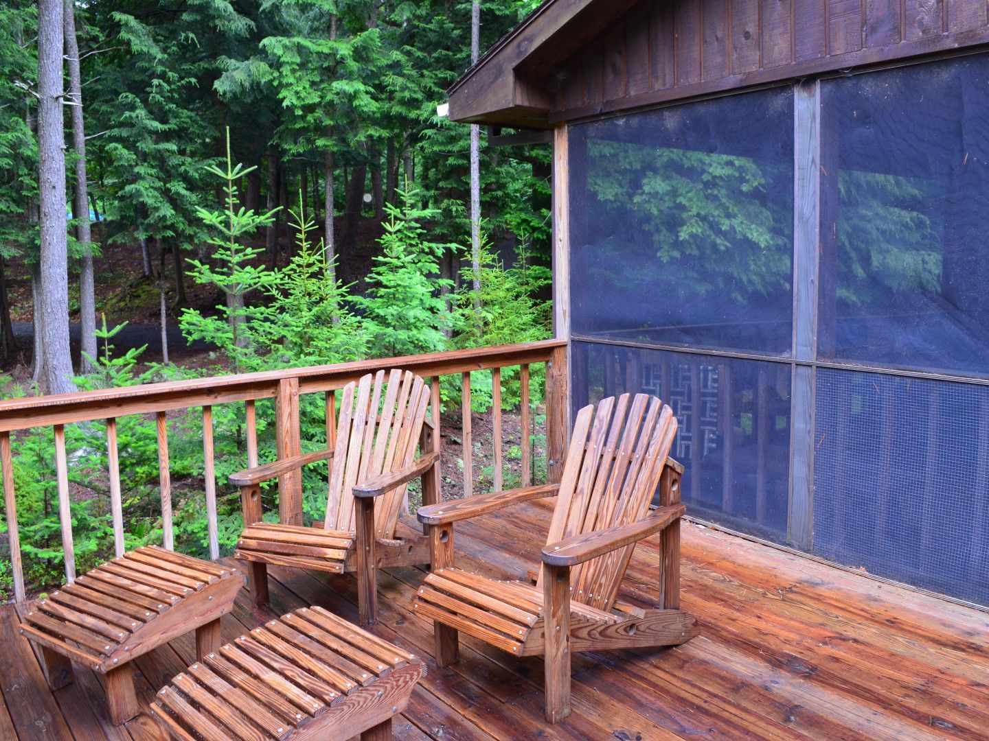 Wooden deck with two chairs overlooking a forest, with a screened porch and cabin wall nearby