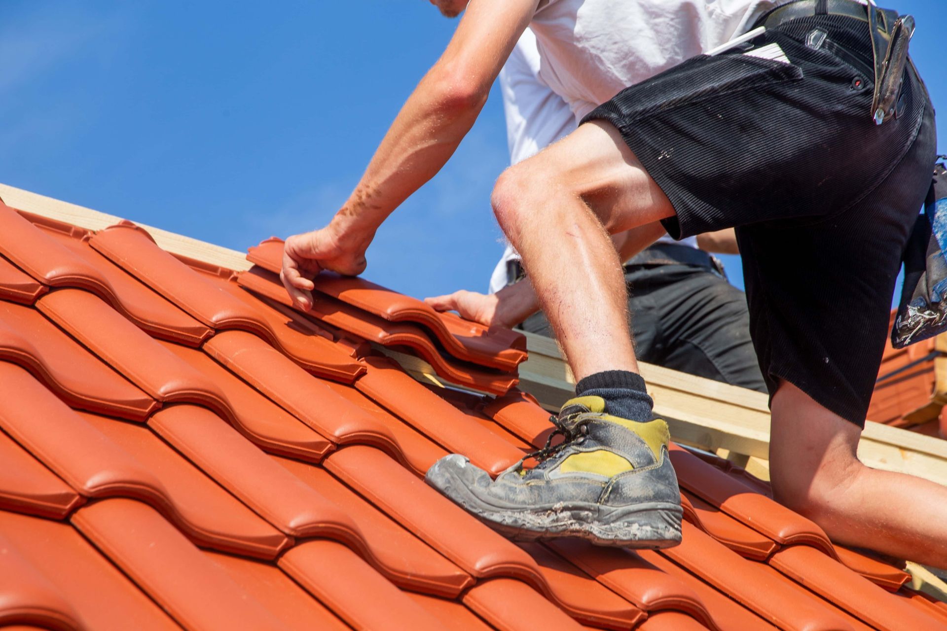 Worker installing red roof tiles on a sloped roof