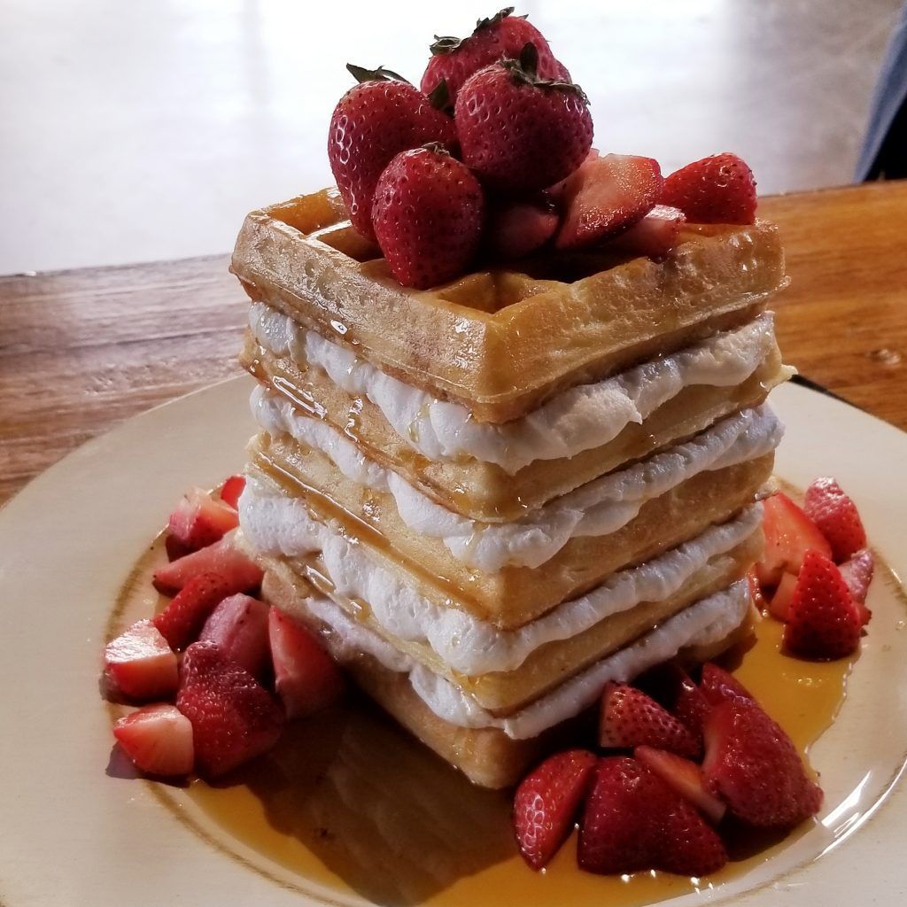 A stack of waffles with whipped cream and strawberries on top