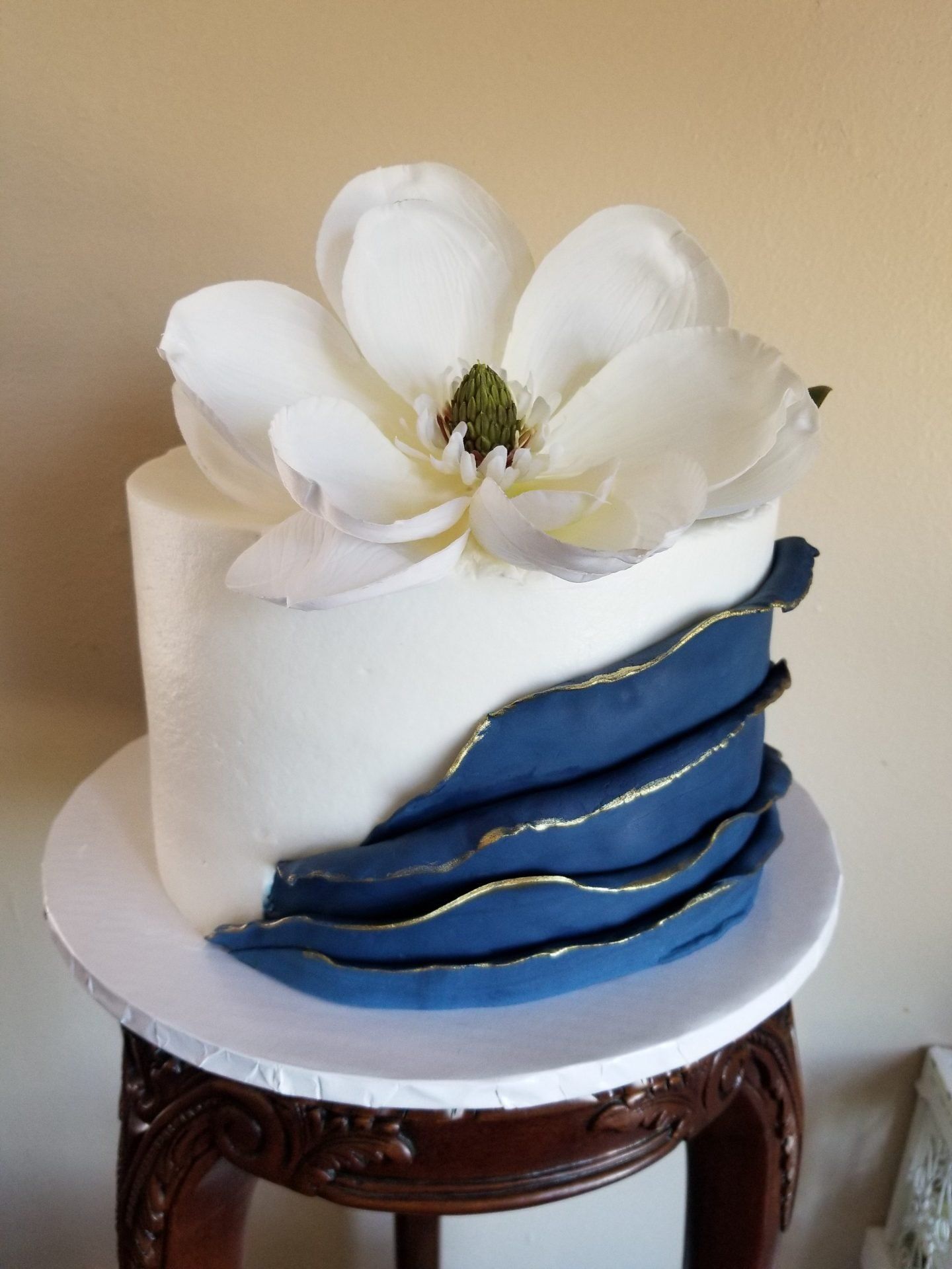 A white and blue cake with a large white flower on top