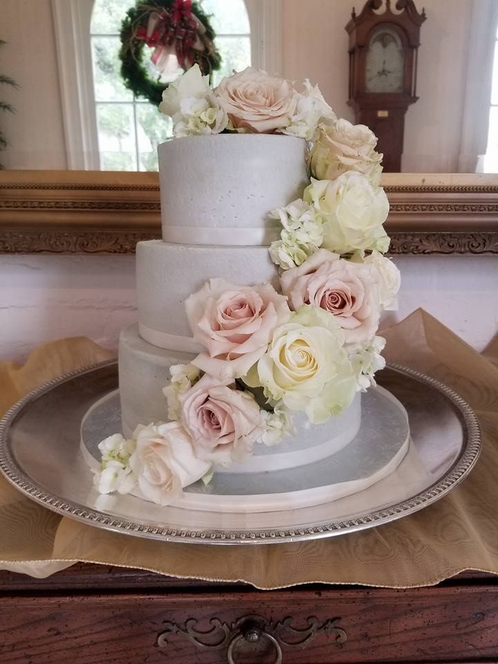 A wedding cake with roses on it is on a plate on a table.