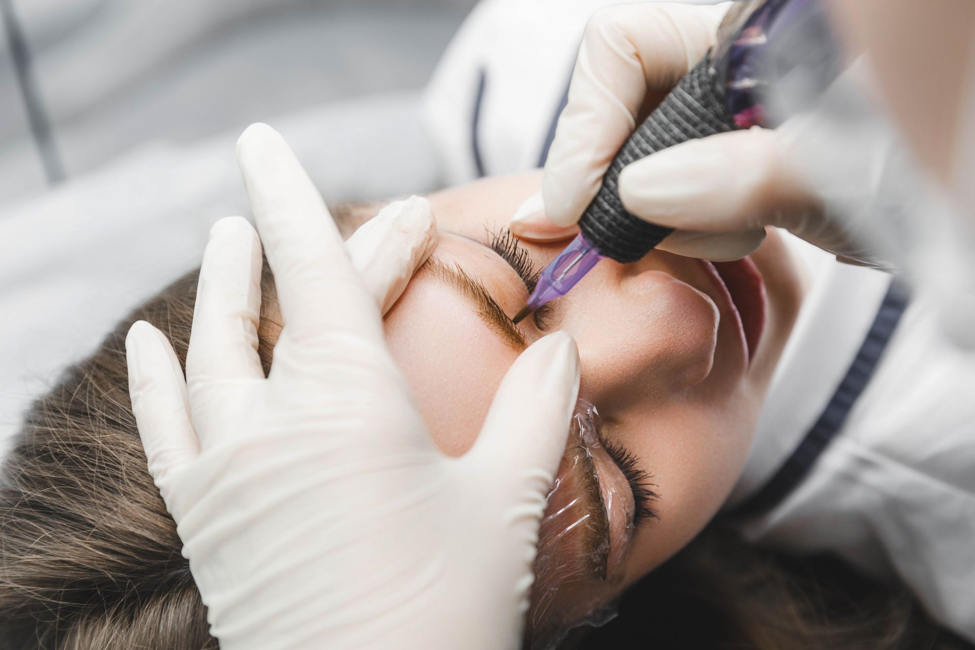 A woman is getting a tattoo on her eyebrows.