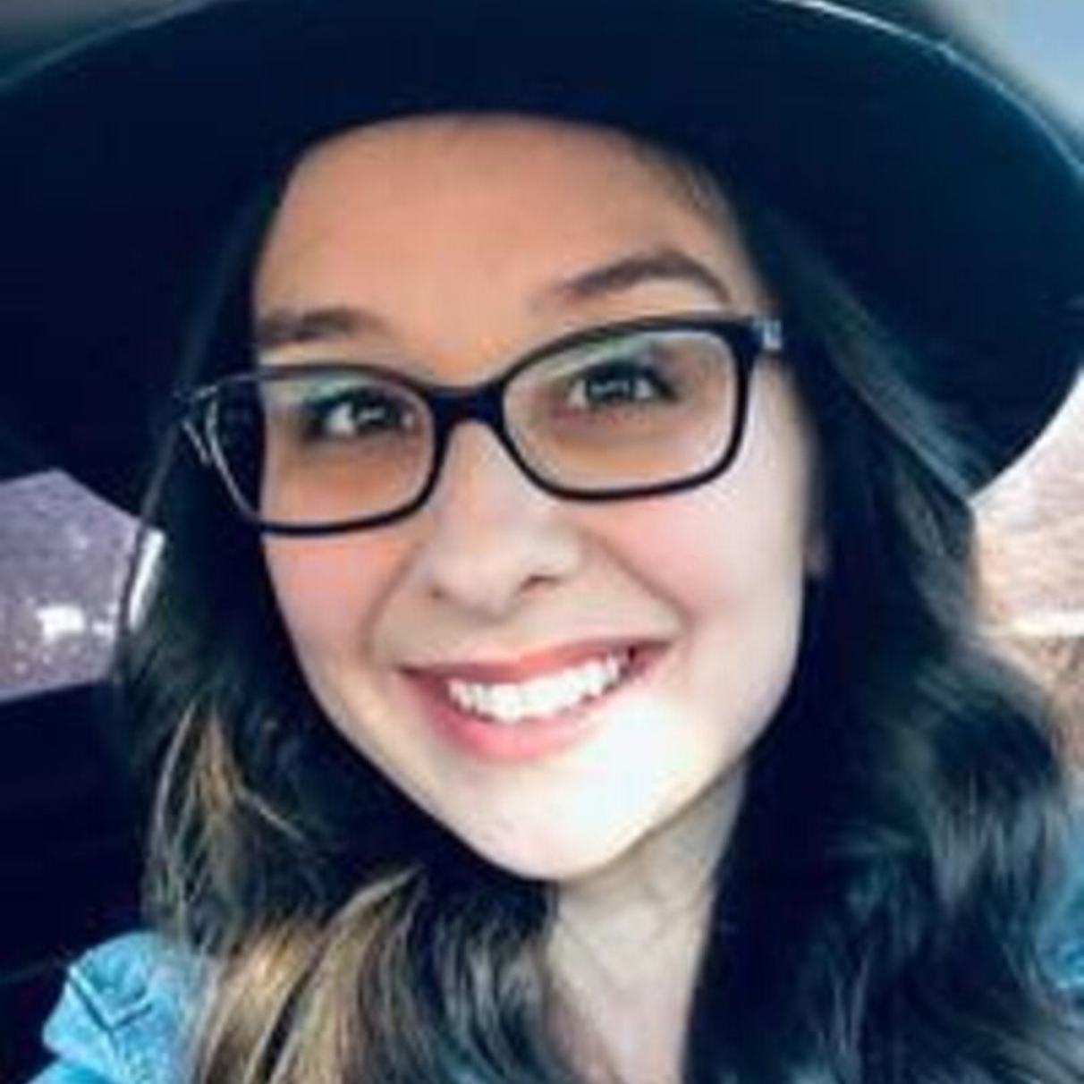 Woman wearing black hat and glasses smiling at the camera.