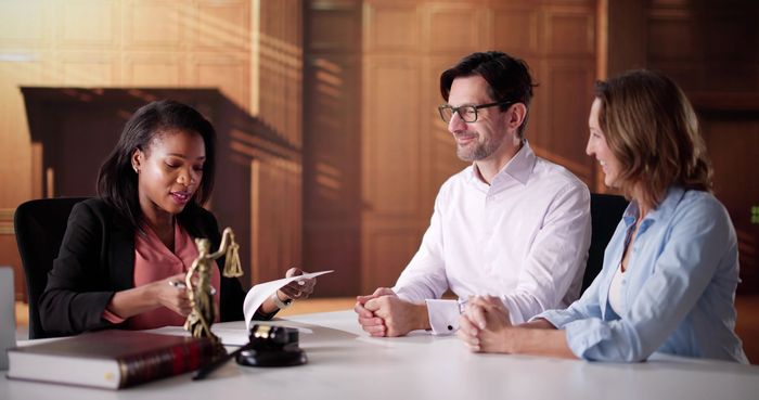  A legal professional reviews documents with two clients seated at a desk in an office setting