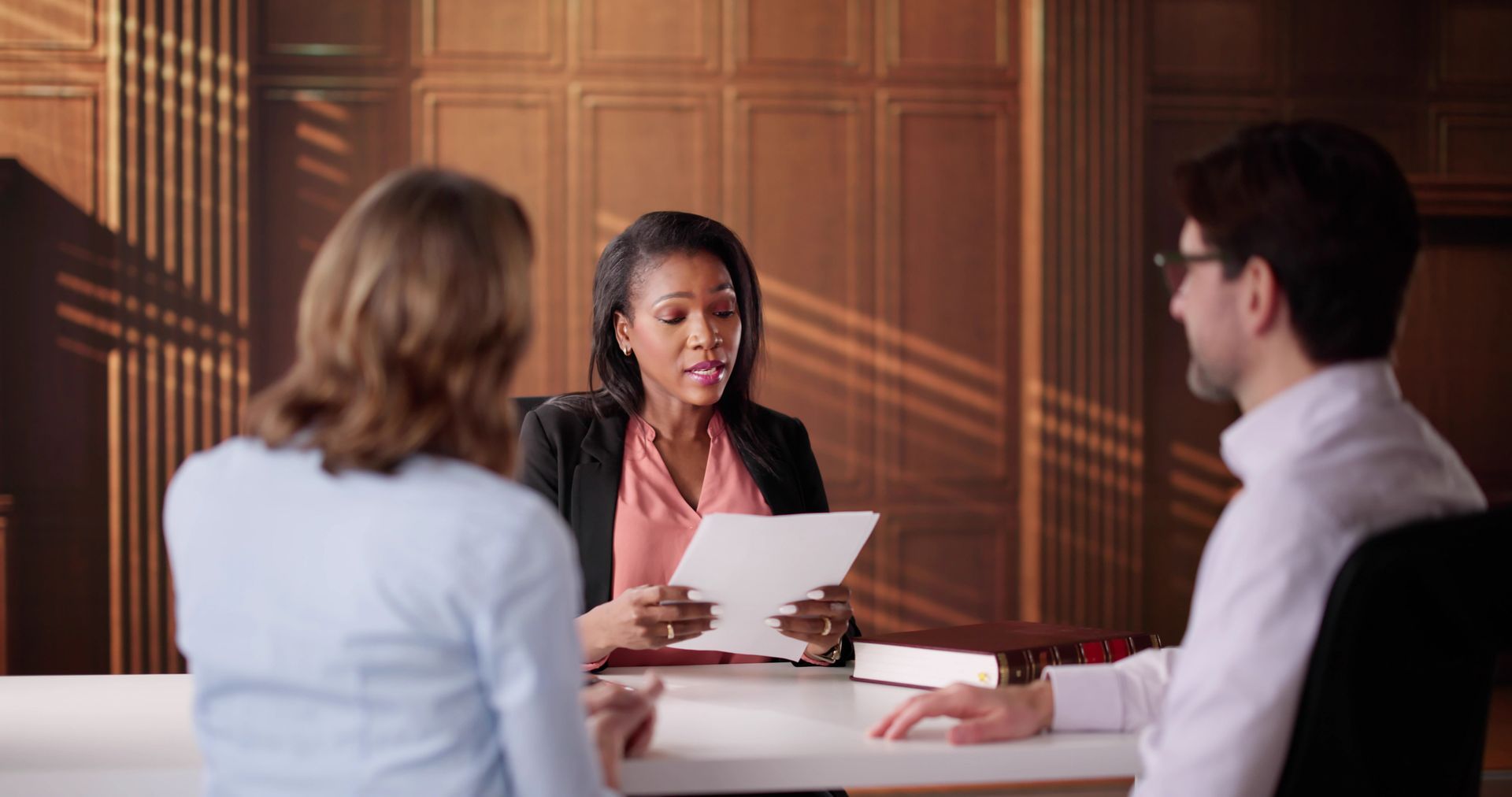 A couple seated at a table speaking with a family law judge holding documents at a divorce court