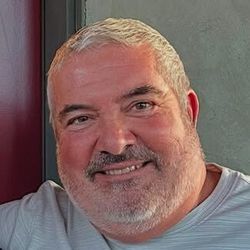 A person with short, light-colored hair and a trimmed beard smiling at the camera.
