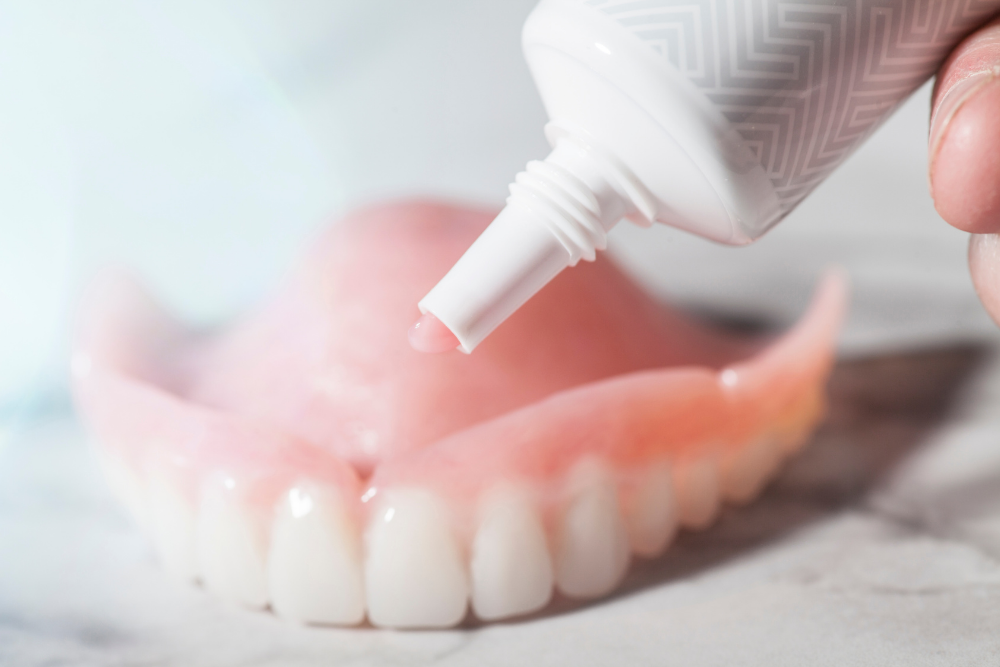 A person is applying toothpaste to a denture.