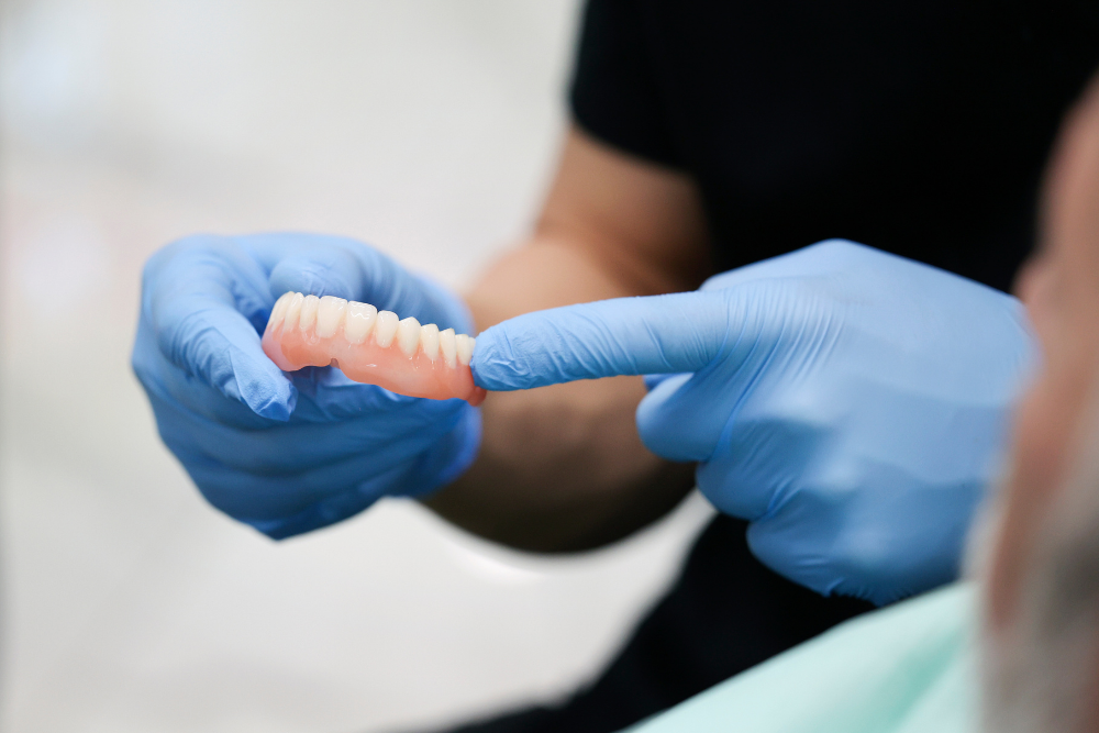 A dentist is holding a denture in his hands and pointing at it.