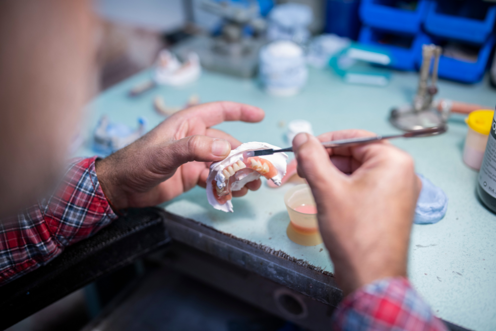 A dentist is working on a denture with a brush.