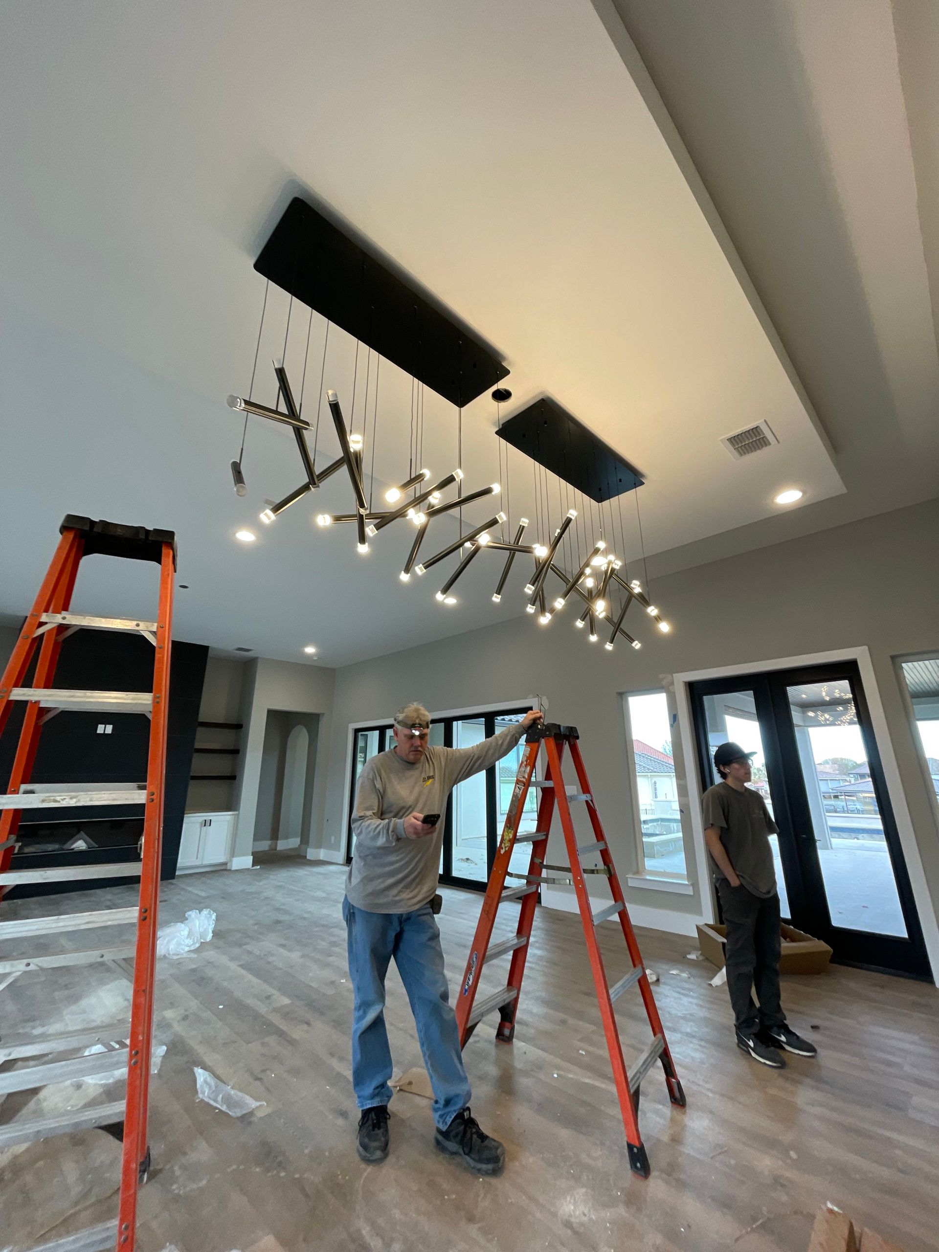 A man is standing on a ladder working on a chandelier.