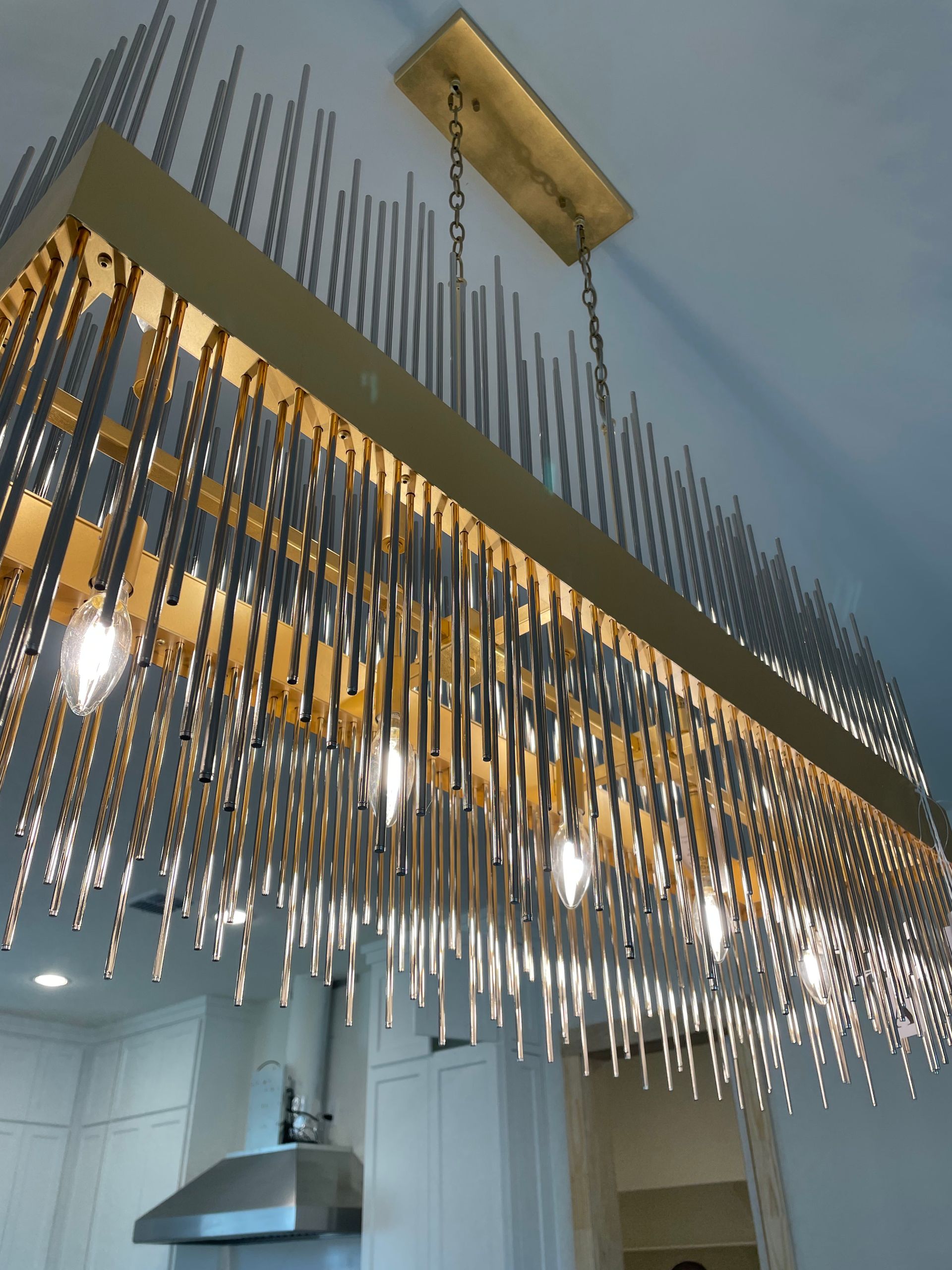 A long chandelier is hanging from the ceiling in a kitchen