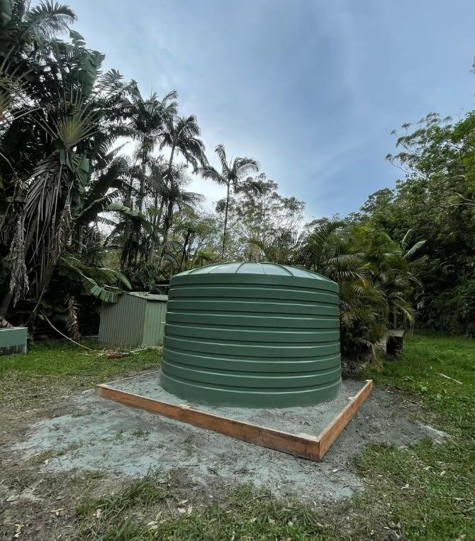 A Green Water Tank is Sitting in the Middle of a Grassy Field — Plumbtek Solutions In Burleigh Heads, QLD