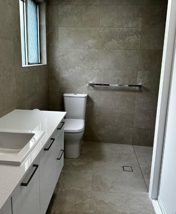A Bathroom With a Toilet, Sink and Window — Plumbtek Solutions In Jimboomba, QLD