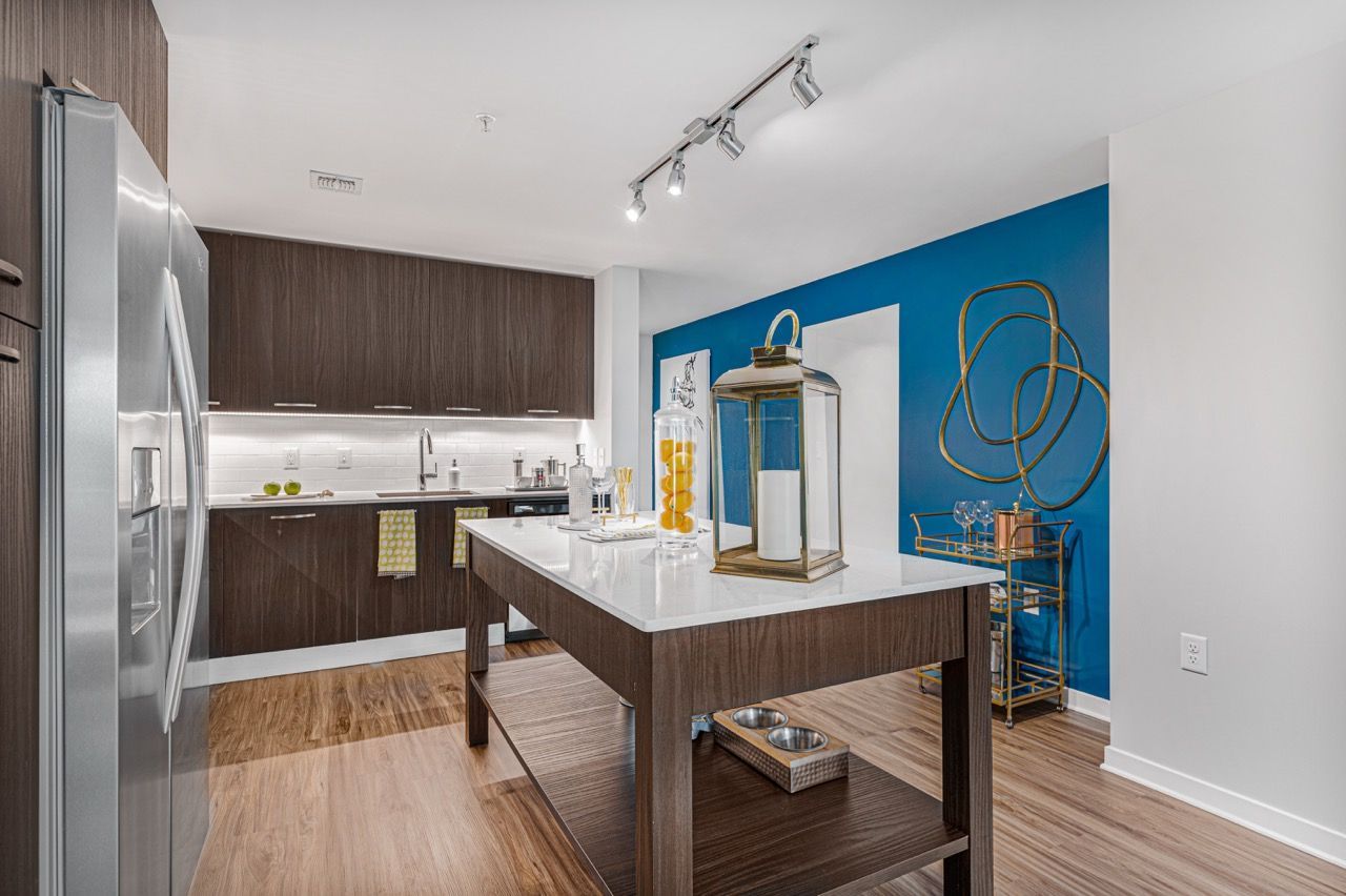 Modern apartment kitchen with dark wood cabinets, stainless steel fridge, and an island.
