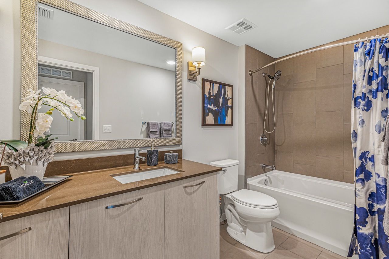 Bathroom with a large framed mirror above a beige vanity, toilet, and tub/shower.