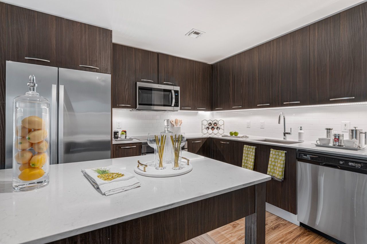 Modern kitchen with dark wood cabinets, stainless steel appliances, and a white island.
