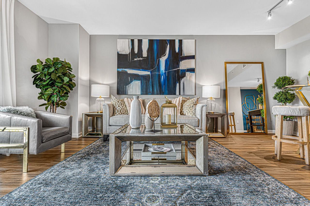 Bright modern living room with gray sofa, glass coffee table, abstract art, and plants.