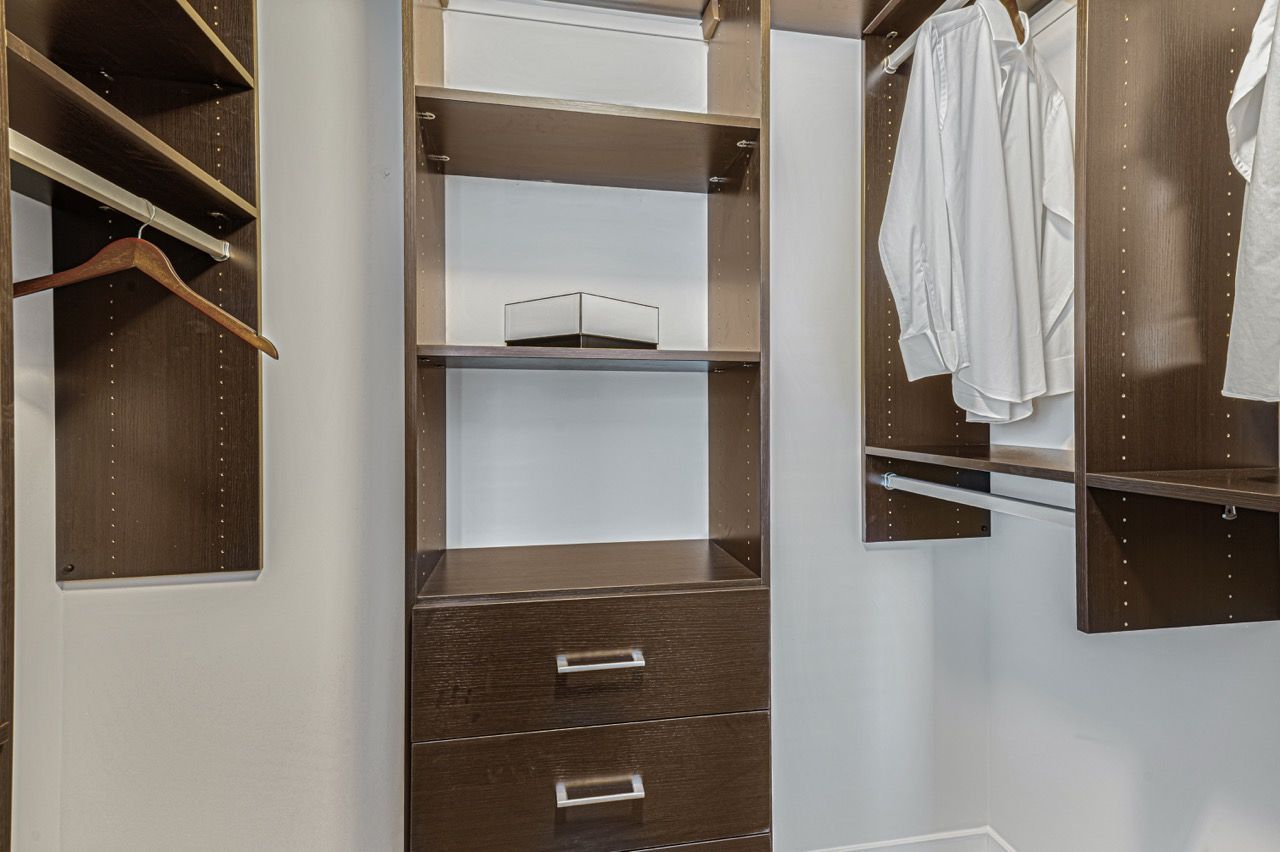 Walk-in closet with dark wood shelving, hanging rods, and drawers.