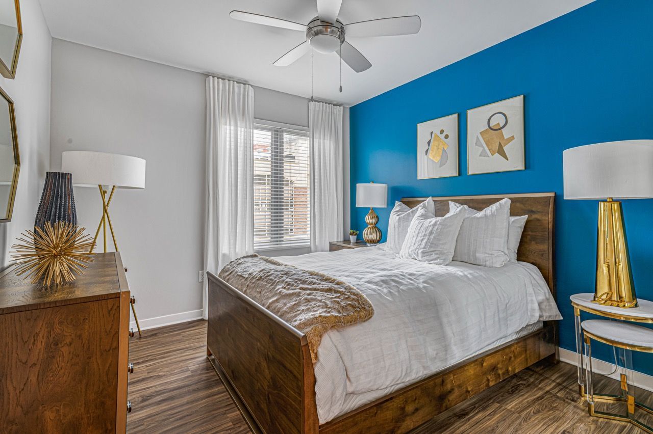 Bedroom with white bedding and blue accent wall, wooden bed frame, two nightstands, and window with white curtains.
