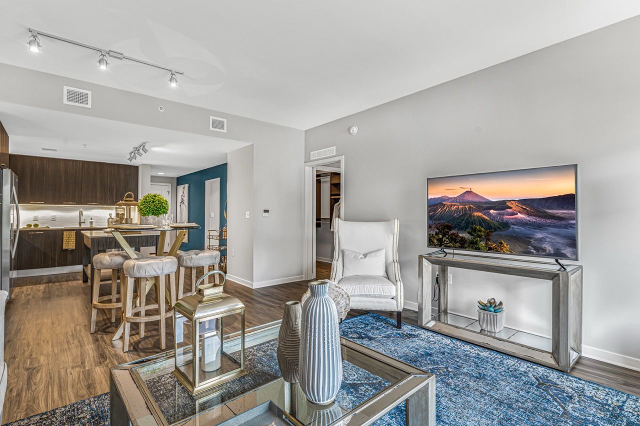 Open-plan living area in a modern apartment with a TV, glass coffee table, and seating.