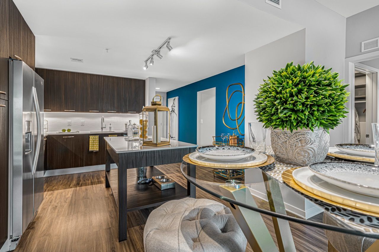 Modern apartment kitchen and dining area with dark wood cabinets, stainless appliances, and a glass dining table.