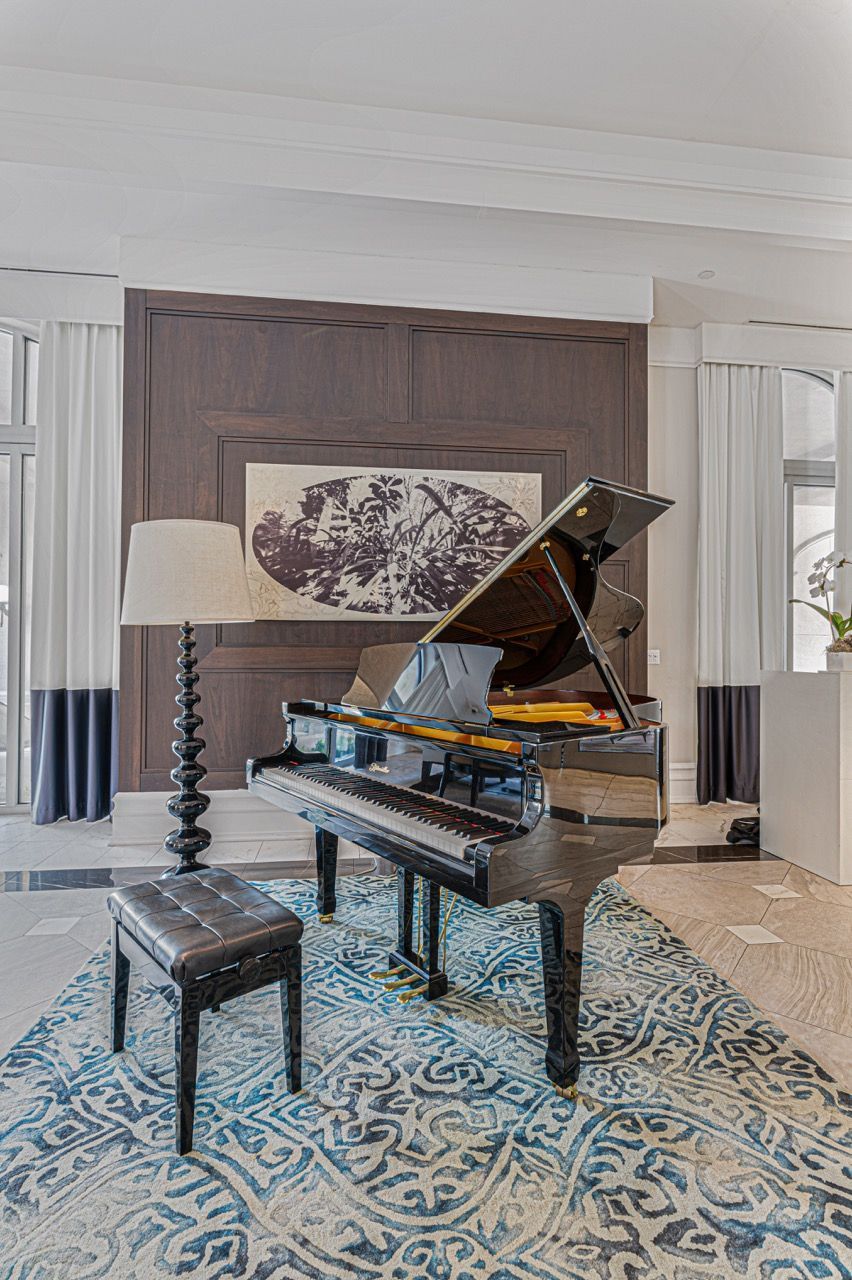 Black grand piano with bench in a stylish, wood-paneled living room.