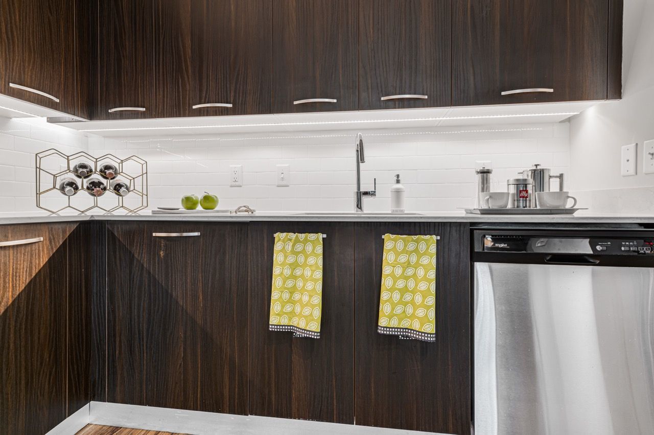 Modern kitchen with dark wood cabinets, white subway tile, and a stainless dishwasher.