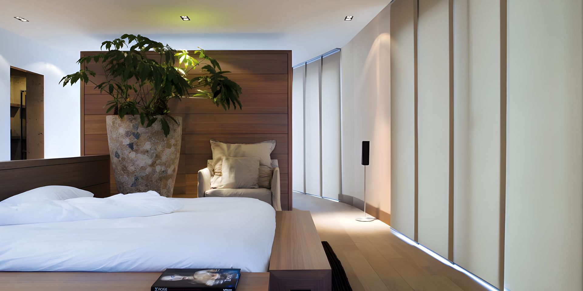 Bed made with white sheet, panel track window blinds visible in the room