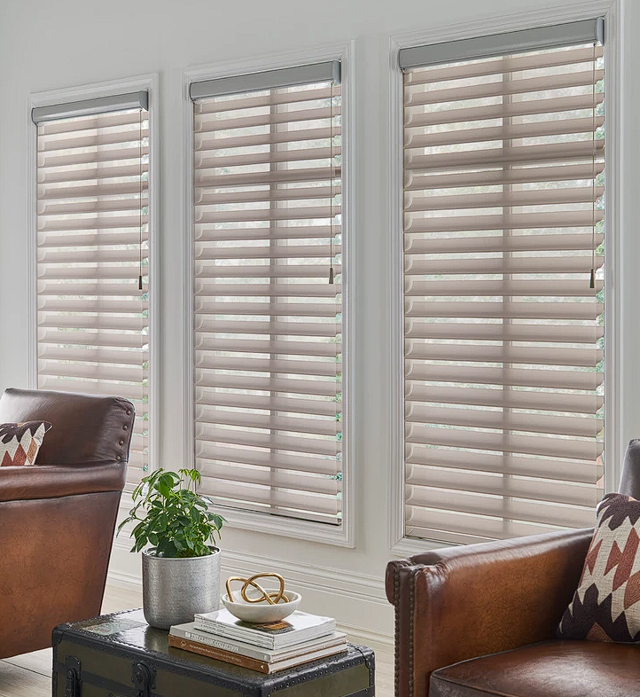 A cozy living room featuring two leather chairs and a coffee table, illuminated by natural light from sheer shades window.